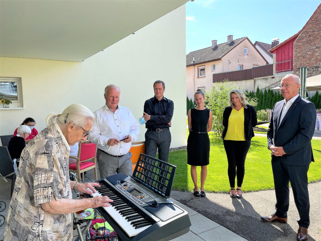 Die 99-jährige Bewohnerin Luise Ehret begrüßte musikalisch die Bundestagsabgeordneten Peter Weiß und Roy Kühne, Hausleiterin Michaela Kalmar, Qualitätsmanagerin Nicola Ipsen und Benevit Grüner Kaspar Pfister (v.l.) beim Besuch im Haus Rheinaue in Wyhl am Kaiserstuhl.