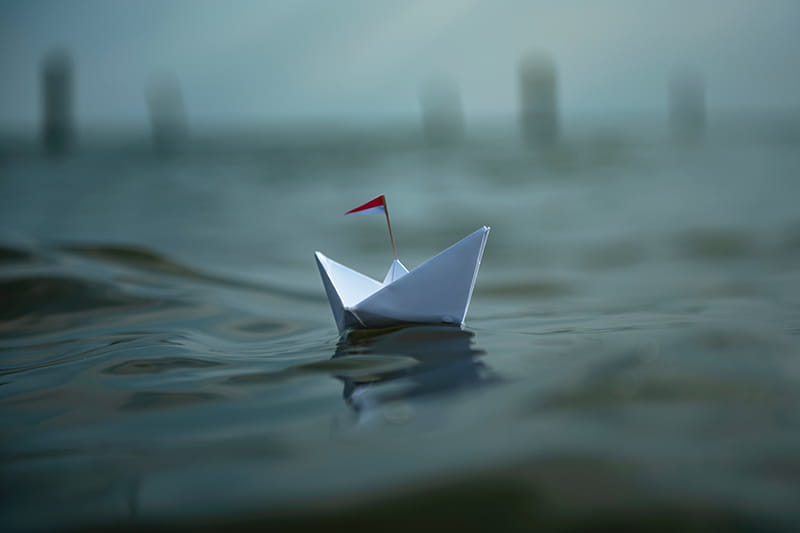 Ein Papierschiff auf dunklem, welligem Wasser.