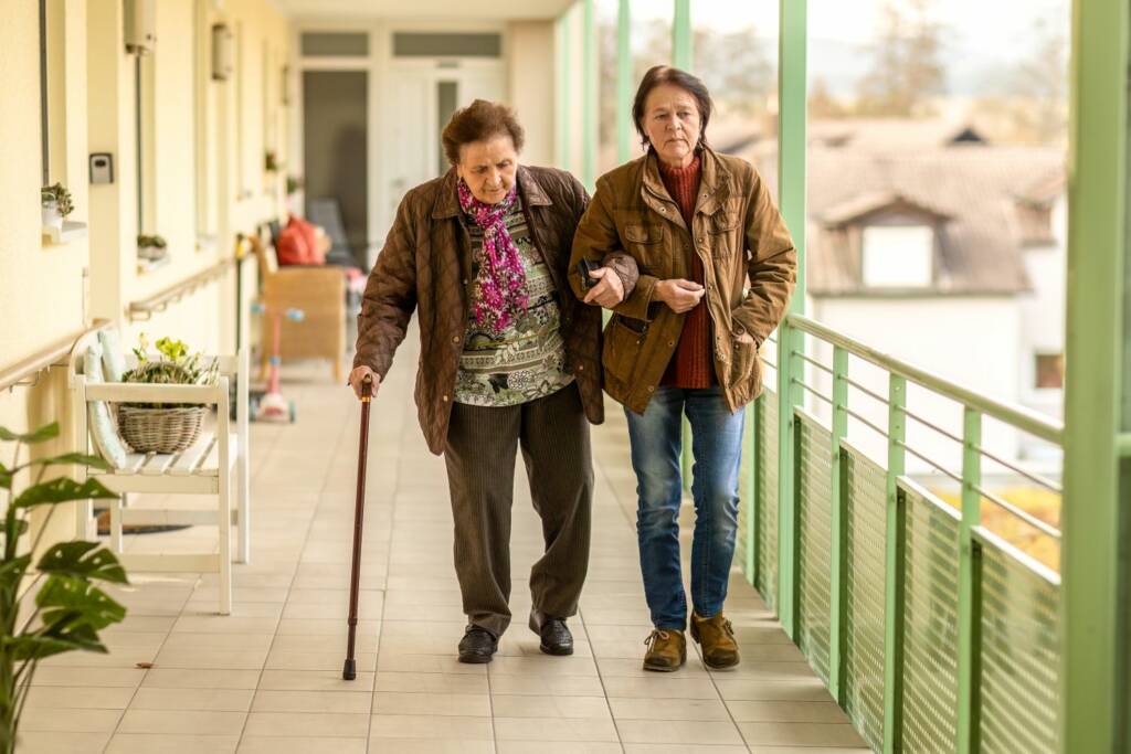 Elderly woman walking with support from her daughter, cane use and fall prevention outdoors